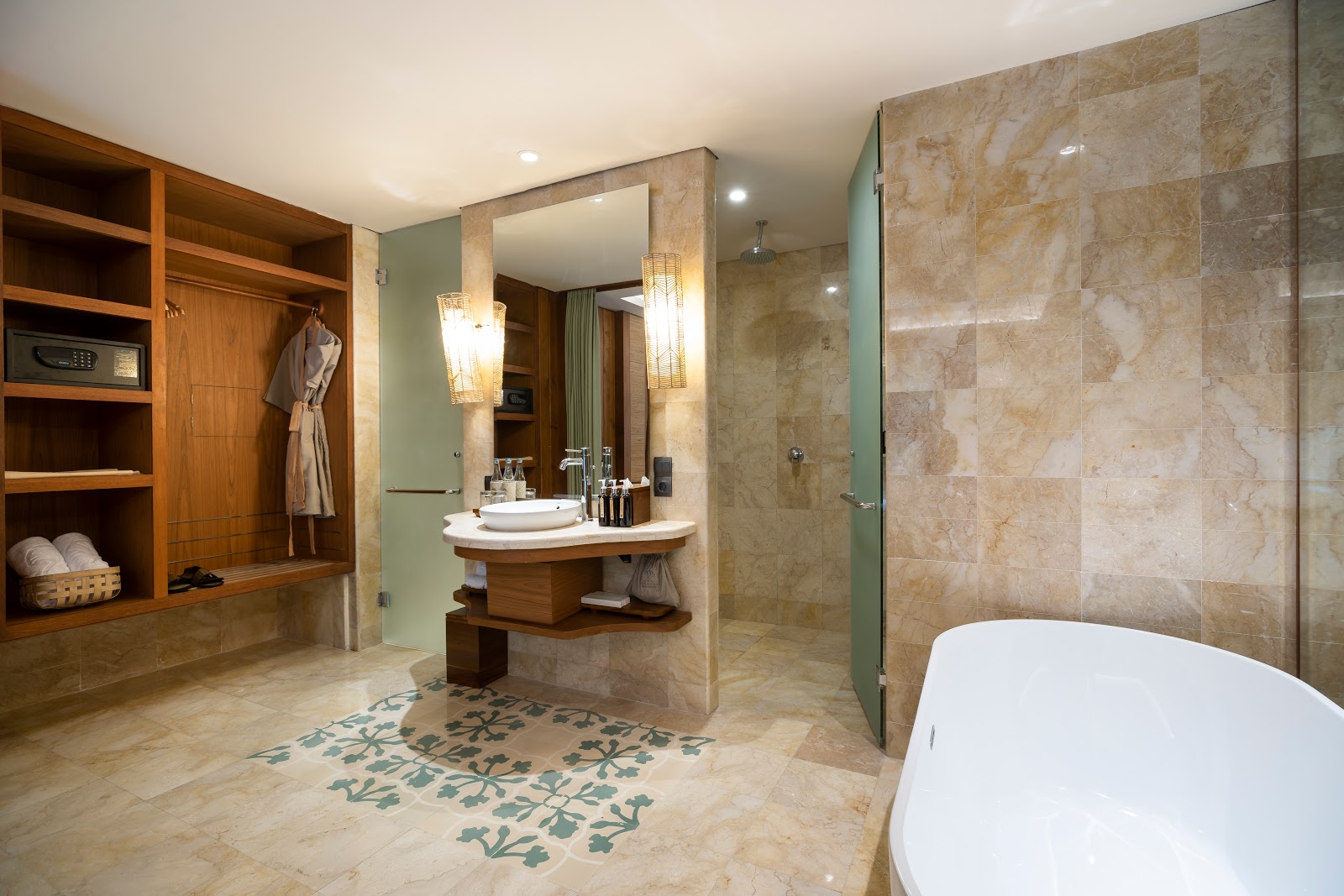 Luxurious spa-style bathroom with marble tiling, wooden vanity with curved sink, large freestanding white bathtub, walk-in shower with glass enclosure, integrated storage shelving, ambient lighting, and decorative floor rug with botanical motif